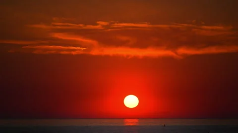 Fiery orange sun setting above the ocean horizon in a peaceful evening scene, 4K Stock Footage 335421917