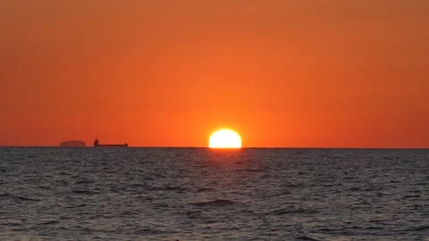Fiery orange sun sinking below the ocean horizon with the silhouette of a cargo 스톡 동영상 342076446