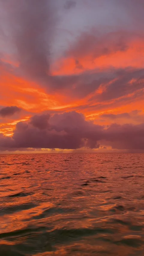 Fiery Orange Sunset Over Calm Ocean Waters with Dramatic Purple Clouds Stock Footage 308661559