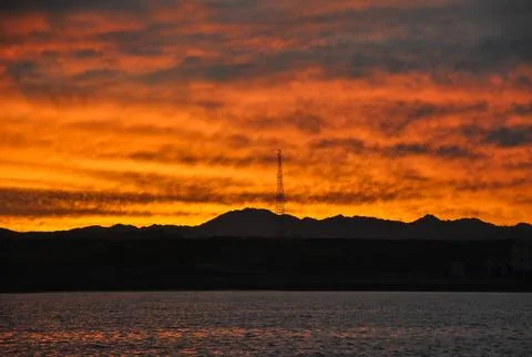 Fiery orange sunset over the Red Sea with dark silhouettes of mountains Stock Photos