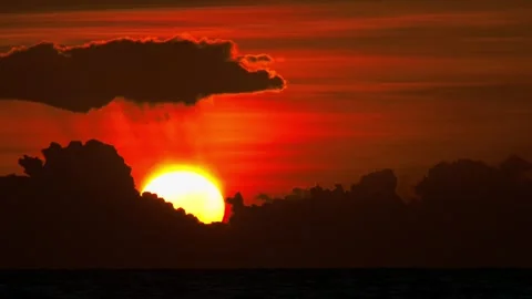 Fiery Red Solar Disc Descending Behind Massive Dark Formations Over Open Water Vídeo Stock 342311805
