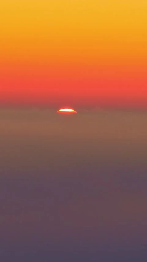 Fiery sun setting below a hazy horizon with a vibrant and colorful gradient sky Stock Footage 339647011