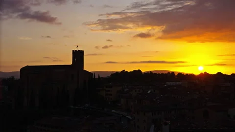 Fiery Sunset Glow Behind Ancient Tower and City Rooftops Stock Footage 256220069