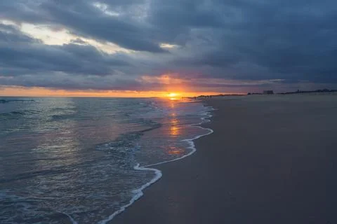 Fiery sunset illuminates the clouds and casts a warm glow over a peaceful bea Stock Photos