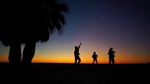 Fiery sunset by the ocean. Figures of a dancing family. Two adults and daughter Stock Footage 82851503