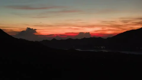 Fiery Sunset over Hills in Bali with Distant City Lights Stock Footage 313976797