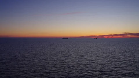 Fiery Twilight Sky Over Calm Ocean with Cargo Ships in Distance (Slow Motion) Stock Footage 309419459