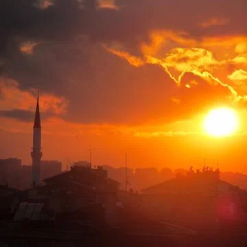Fiery urban sunset with dramatic clouds and a silhouette of a mosque minaret Stock Photos