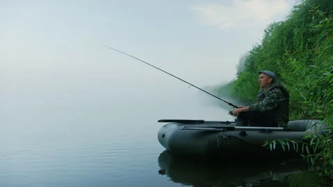 A fifty-year-old man sits in an inflatable boat while fishing on the lake Stock Footage 251731638