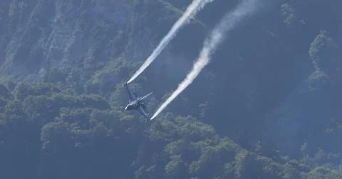 Fighter Jet Doing Aerobatic Maneuver With Smoke Trails Over Forested Mountain Stock Photos