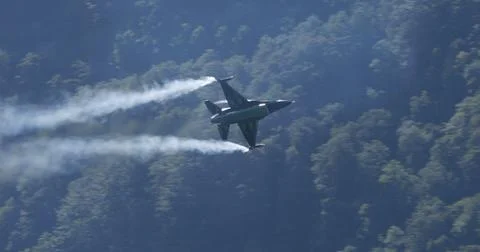 Fighter Jet Performing Sharp Banking Maneuver Over Forested Mountain Scenery Stock Photos