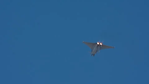 Fighter jet with twin afterburner glow flying against blue sky Stock Footage 334347575