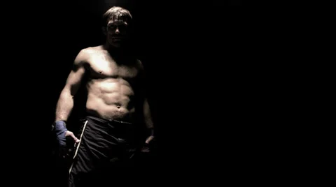 A fighter shadow boxes with the camera under a light in a dark room Stock Footage 33866445