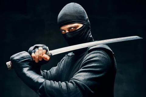 Fighting ninja posing with a sword over black background Stock Photos