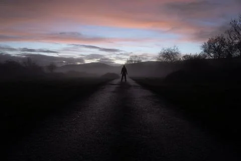 A figure back to camera on a road heading into the sunset Stock Photos