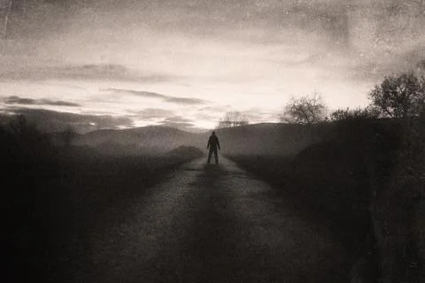 A figure back to camera on a road heading into the sunset on a moody evening Stock Photos