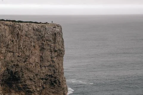 A   figure   on   a   cliff   overlooking   the   ocean   under   a   grey Stock-Fotos
