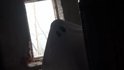Figure dressed as ghost hides in corner, leans forward with curiosity, black Stock Footage 320246722