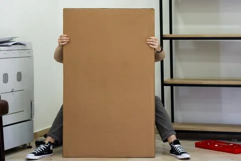 Figure gripping sides of vertical flat-pack furniture box in office Stock Photos