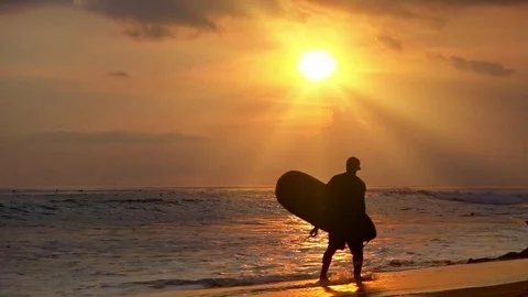 Figure of man walking along surf line and carrying surfboard against sunset sky Stock Footage