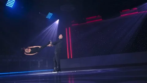 Figure skaters pair performs stationary rotational lift in spotlight. Man holds Stock Footage 171690875