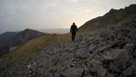 A figure walking over rocks towards a wild camping tent in the mountains Stock Footage 245113260