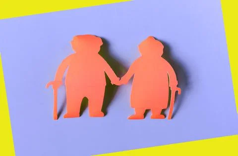 Figures of two elderly people made of red cardboard on a colored background. Stock Photos