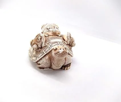 Figurine of a turtle with three frogs on a shell on a white background. Stock Photos