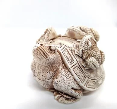Figurine of a turtle with three frogs on a shell on a white background. Stock Photos
