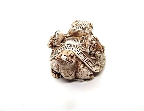 Figurine of a turtle with three frogs on a shell on a white background. Stock Photos