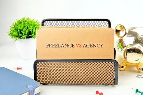 A file folder labeled Freelance versus Agency stands in a mesh desk organizer Stock Photos