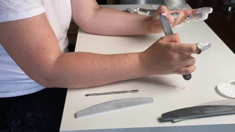 Filing nails and removing gel polish with foil wraps on fingertips. woman Stock Footage 317153883