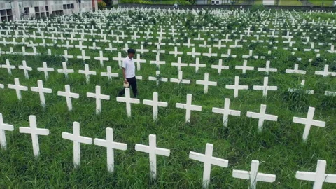 Filipino boy walking through rows of crosses in a cemetery 库存影片 334370722