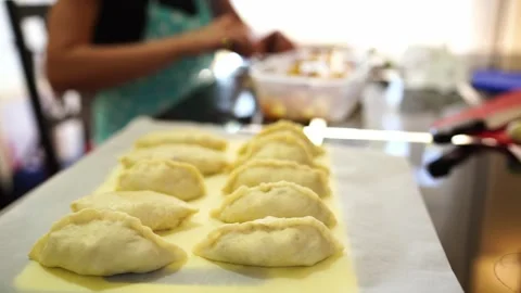 Filled pies lie on a baking sheet next to the chef stuffing pieces of dough Vídeos de archivo 282614762