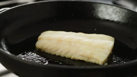 Fillet of cod sizzling in a hot cast iron pan, camera slides left Stock Footage 92148910