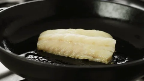 Fillet of cod sizzling in a hot cast iron pan, camera slides left Stock Footage 92150281