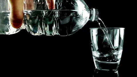 Filling a drinking glass with water with bubbles through bottle on black back Stock Footage 77373131