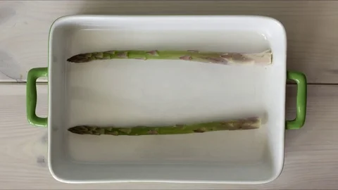 Filling emptying casserole baking oven-pan dish with green spring asparagus Stock Footage 75746531