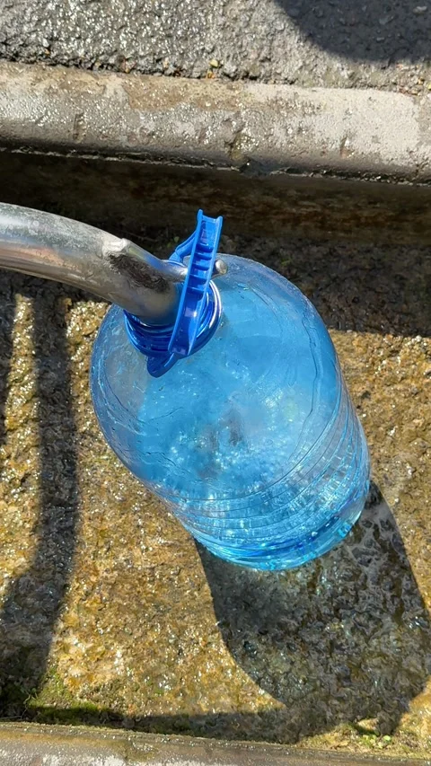 Filling a large blue water container with fresh spring water from an outdoor Stock Footage 345180938