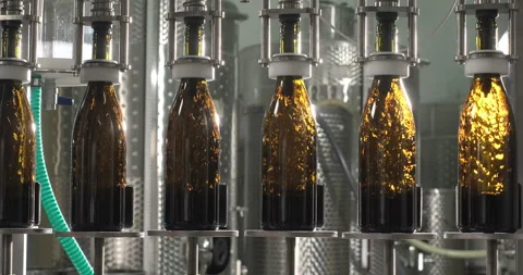 Filling red wine by the machine into bottles made of green glass. Wine bottling Stock Footage 247961067