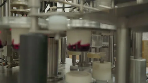 Filling small plastic cups with jam then yogurt. Automated production line Stock Footage 150123373