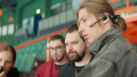 Film director with headset instructs crew at sports stadium Видео 303068635