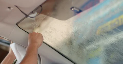 The film installer is using a glue scraper to scrape the old glue off the glass. Stock Footage 282695178
