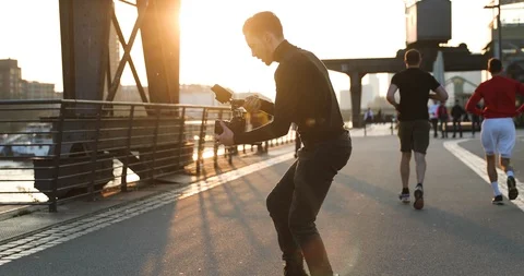 Filmmaker camera handheld on sunset in a big city. People run in background Stock Footage 126861182