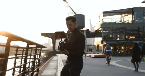 Filmmaker camera handheld on sunset in a big city. People run in background Stock Footage 126861264