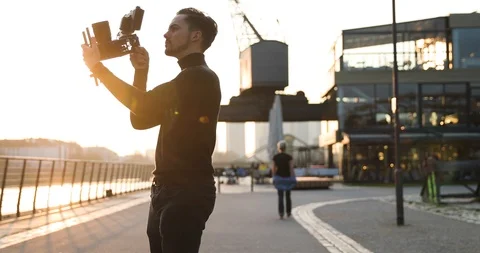Filmmaker camera handheld on sunset in a big city. People run in background Stock Footage 126862716