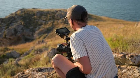 Filmmaker with camera on tripod changes settings and shoots a sea sunset. Stock Footage 203788430