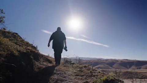 Filmmaker Walking With Camera Along Sunlit Hillside Trail in Rural Tucuman Stock Footage 339754153