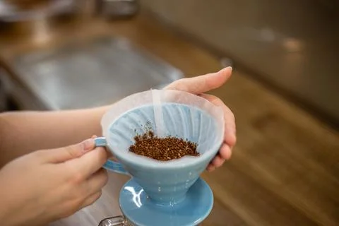 Filter with ground coffee in funnel in focus. Drip filter coffee brewing. Stock Photos