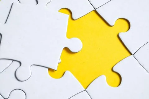 Final missing white piece lies on jigsaw puzzle on yellow background. Stock Photos